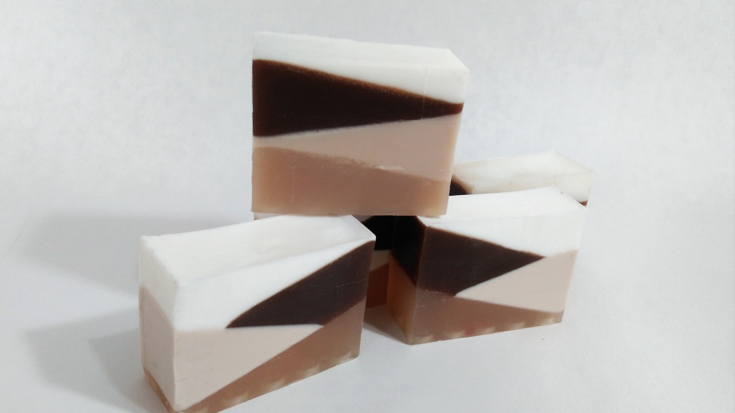 Karamelvoé mydlo v troch kúskoch v odtieňoch hnedej farby stojí uložené na sebe na bieom pozadí.